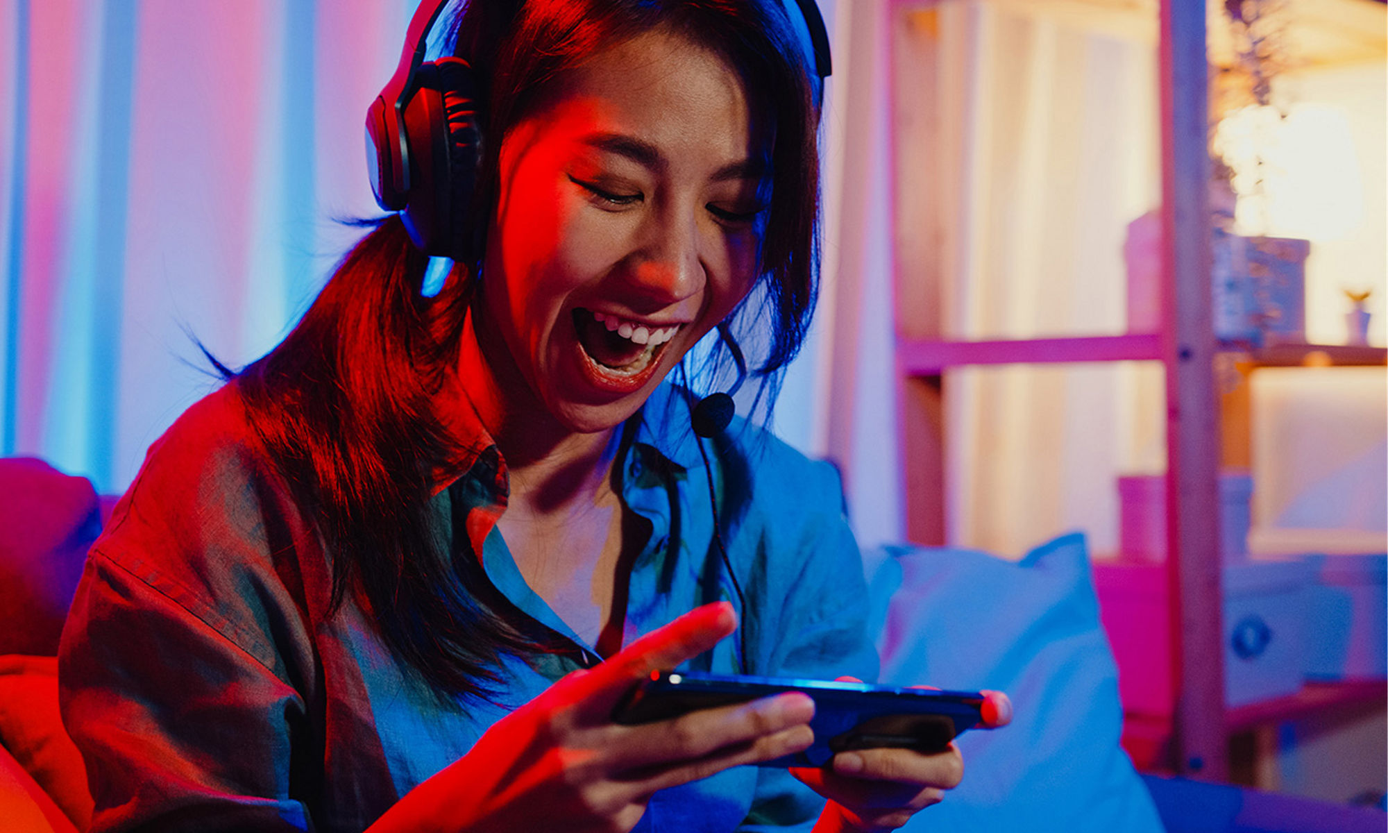 Female wearing headphones and looking down excitedly at a device she is holding