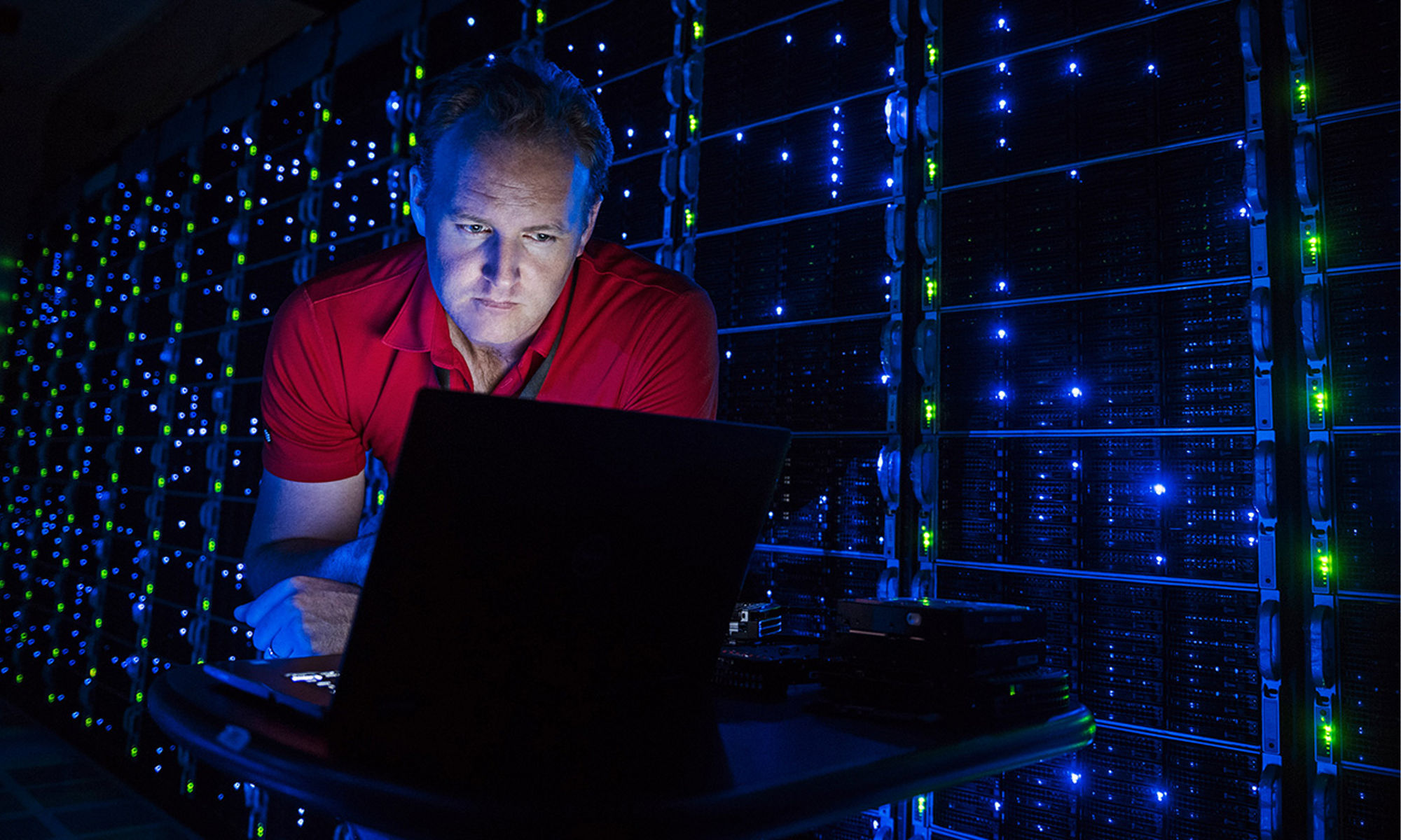 A working at a laptop in a dark server room