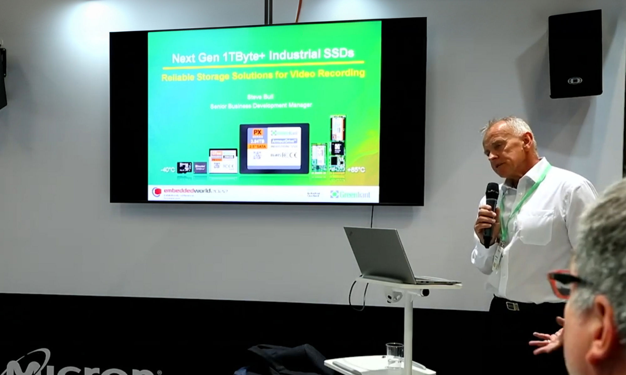 Man presenting with a microphone and a green monitor in the background