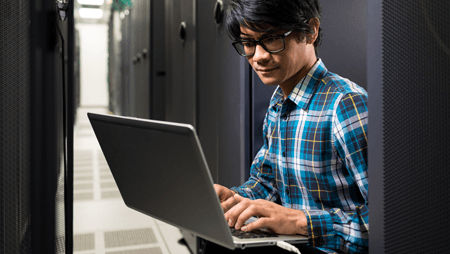 Technician using a laptop in a data center, linked to Micron's high IO performance with Microsoft Storage Spaces Direct